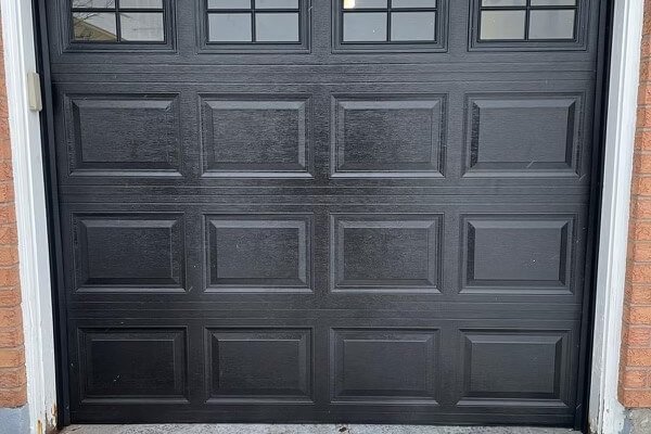 black square garage door with windows against brick facade with skylight and concrete driveway